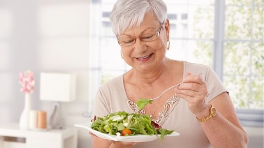 An older woman eating a healthy salad consisting of foods rich in antioxidants and fatty acids. 