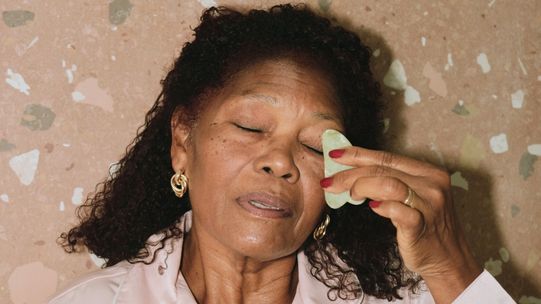 An older woman using a gua sha tool to massage smile lines. 