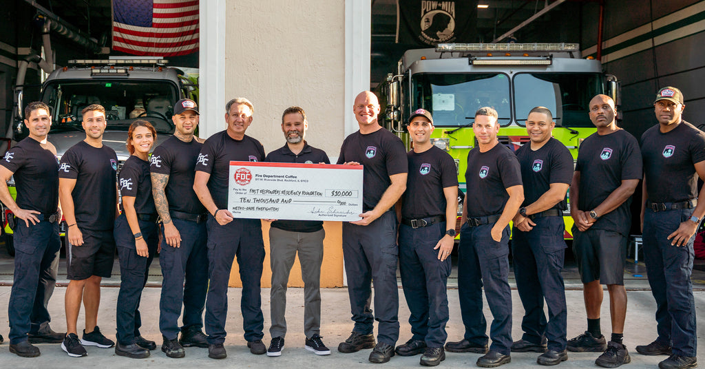 Group of firefighters standing together holding an oversized donation check in front of a fire station.