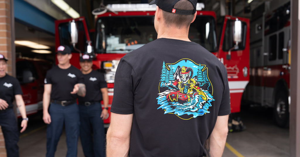 The back of a firefighter and other firefighters standing in front of a firetruck.,