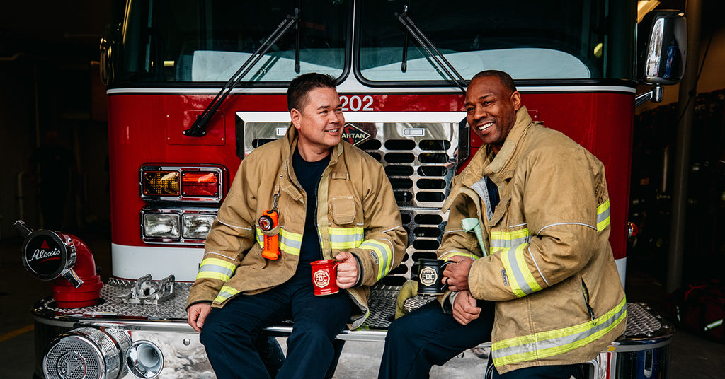 Firefighters sitting together in front of a fire truck having coffee.