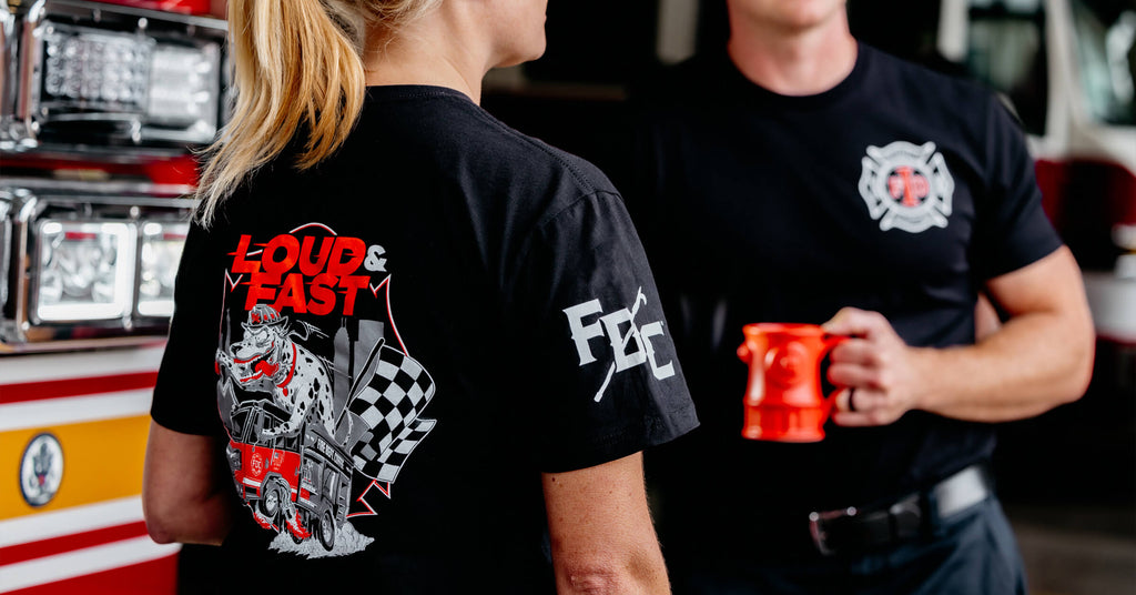 Back of a female firefighter wearing a custom-design t-shirt, standing next to male firefighter that is holding a coffee mug.