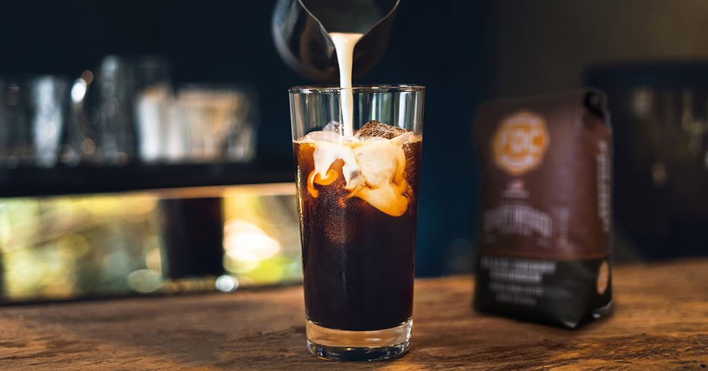 Glass of iced coffee with cream being poured