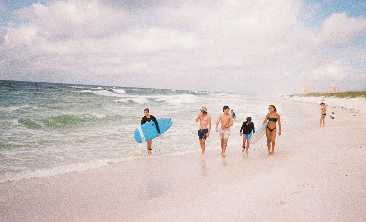 A group of people walking on the beach, with one holding a blue Waterboyz surfboard.