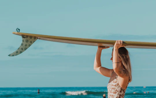 Woman in a swimsuit holding a longboard with a spotted single fin from Waterboyz at the beach.