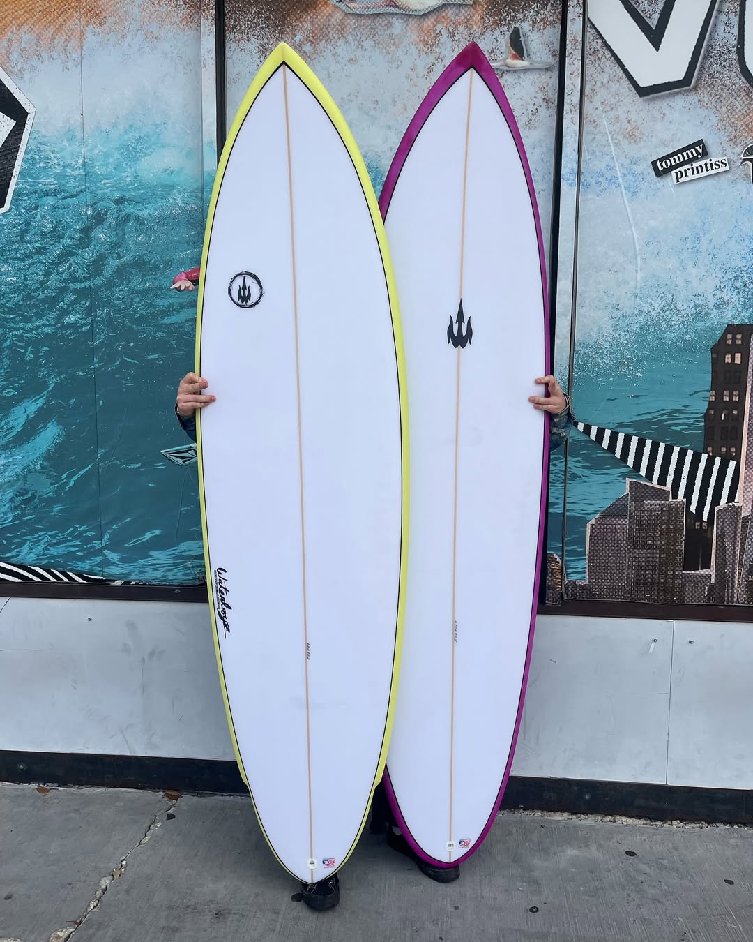 'Two surfboards: one with a yellow edge and the other with a purple edge from Waterboyz.'