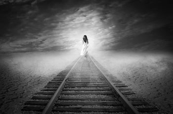 A black and white photo of a woman walking away from the viewer while on train tracks: Anna Karenina Isn't Dead
