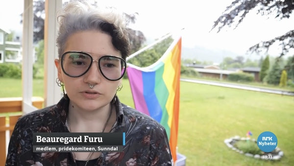 A still of Beauregard Furu aka Bo Starsky being interviewed by NRK TV station, a wide lawn and a Pride flag behind them
