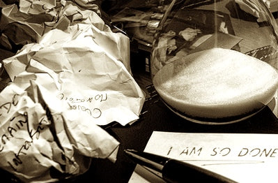 A pile of crumpled paper besdie an hourglass, beneath them is a pen resting on a pad of paper on which are the words "I am so done."