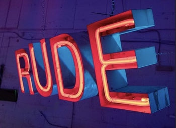 Photo of the word 'RUDE' done up in orange-red neon with the rest of the image having a purple-dark background