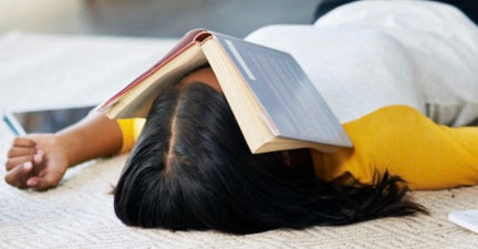 An image of a black woman lying on her bed arms out to the side with a book over her face