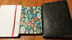 An array of three notebooks, from white to flowered to black