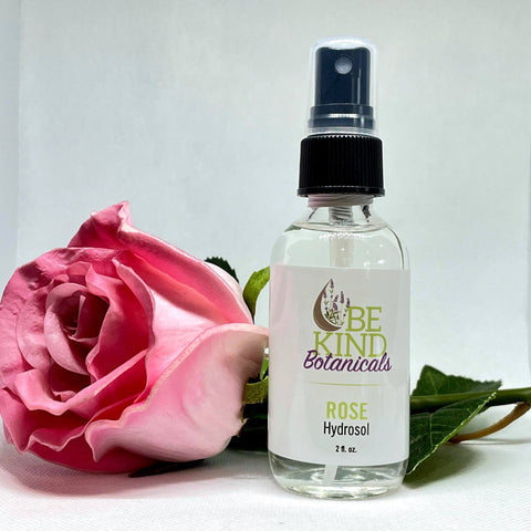 A Pink rose behind a spray bottle with label reading "Rose Hydrosol" from Be Kind Botanicals 
