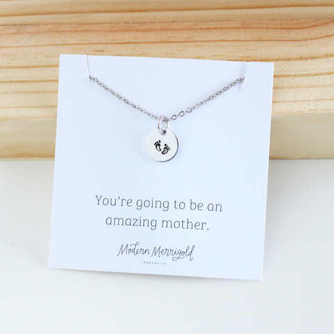 Photo of silver necklace with imprinted baby feet on charm. Text on the card "you're going to be an amazing mother" reads "
