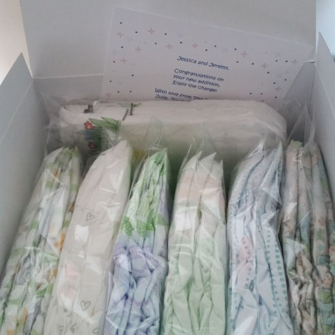 Picture of a white box with 7 Diaper Sample Packs of various brands. Gift message card is partially visible tucked into box reading "Jessica and Jeremy, Congratulations on your new addition. Enjoy the change!