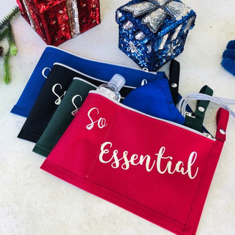 Set of 3 zippered pouches in blue, black and red with "so essential" printed on the bags. Background of gift wrapped boxes in blue and red