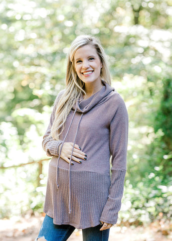 Pregnant blond model wearing a long mauve maternity sweatshirt with a cowl neck.