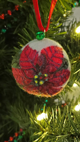 A poinsettia flower is felted to a white felt ball.  A green jingle bell and a red ribbon are used to hang them.  