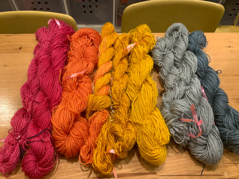 spread of 9 mini-skeins of yarn in varying shades of yed, orange, yellow and blue-green