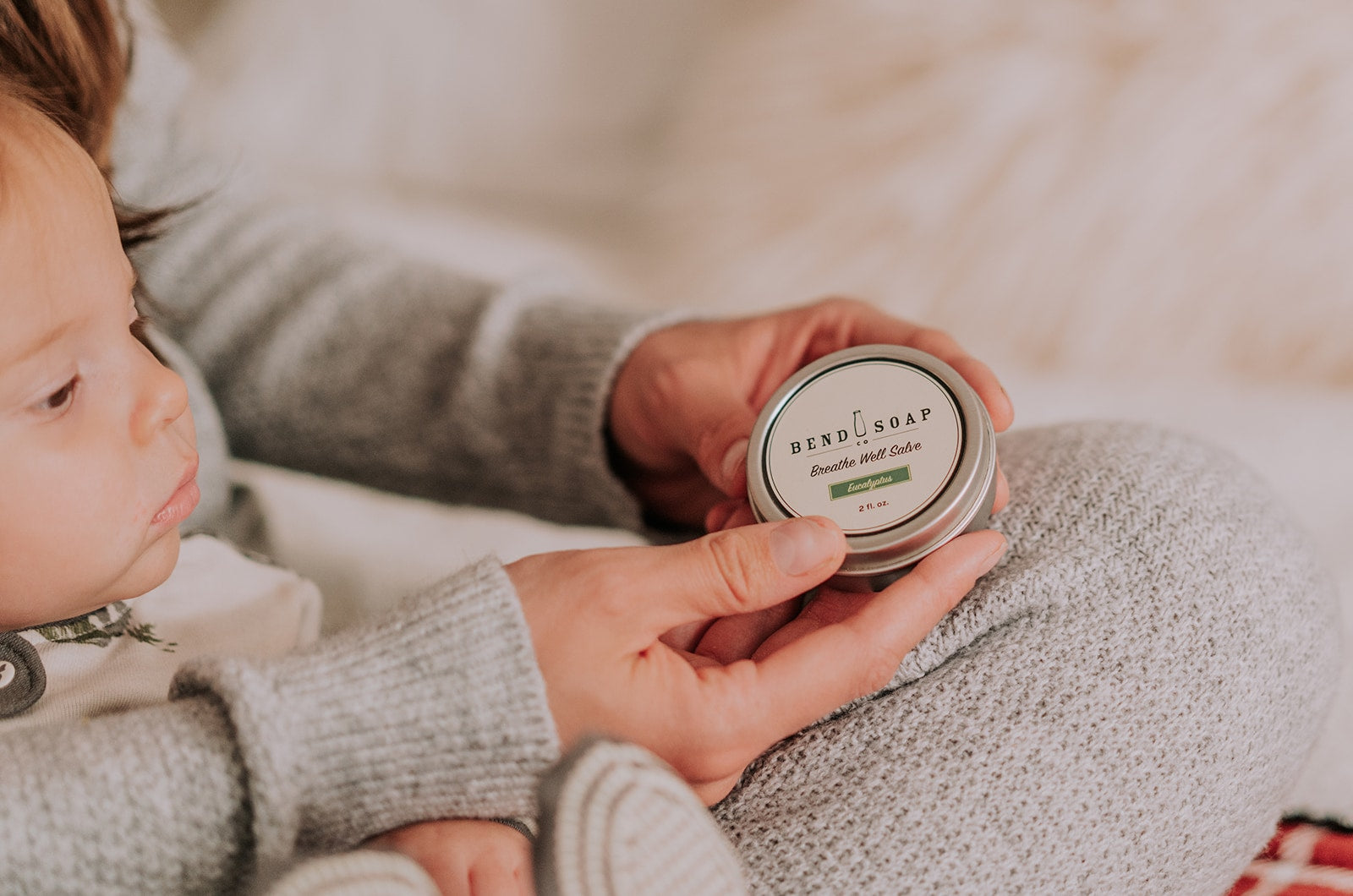 a woman holds a tin of breathe well salve in her hands to apply it to her child's chest