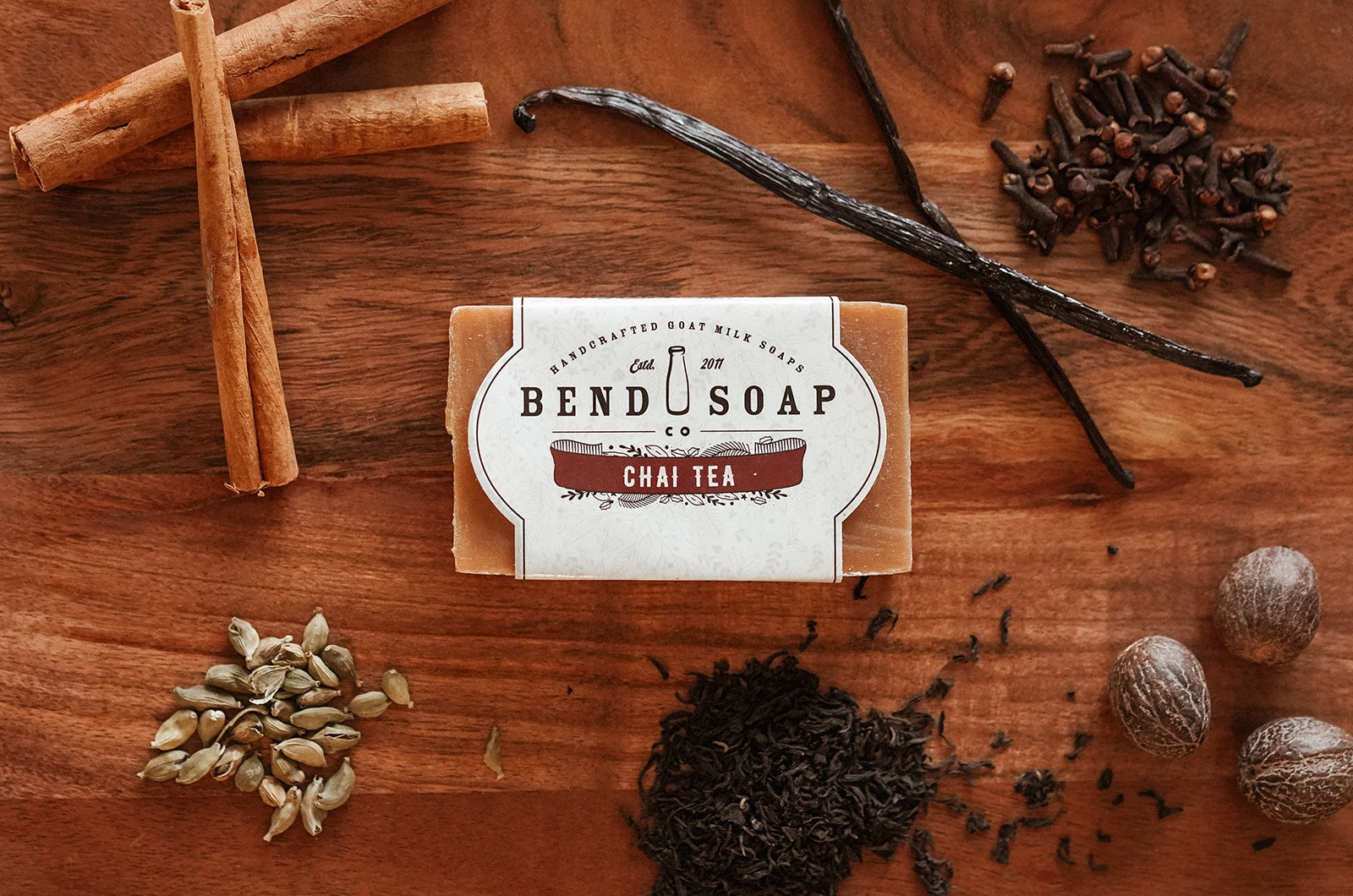 Seasonal Chai-Tea goat milk soap on a wooden board surrounded by fresh cinnamon, clove, vanilla and more