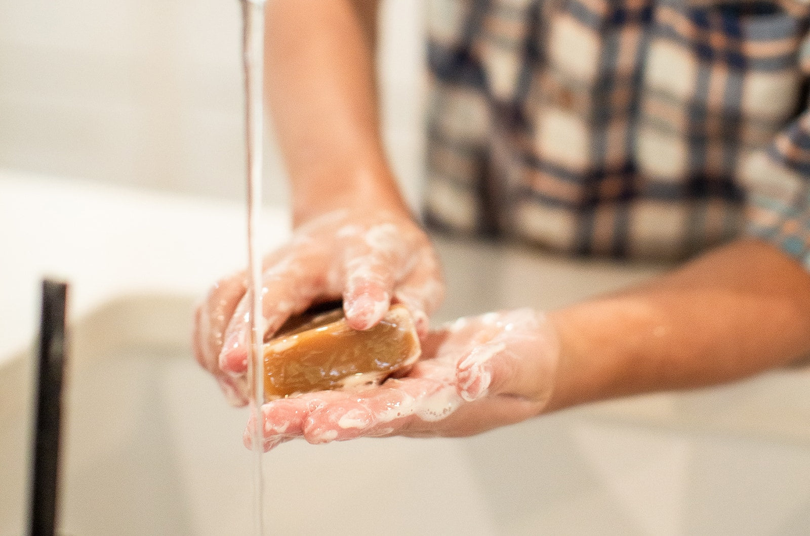 Young boy lathering goat milk soap in his hands over a white sink