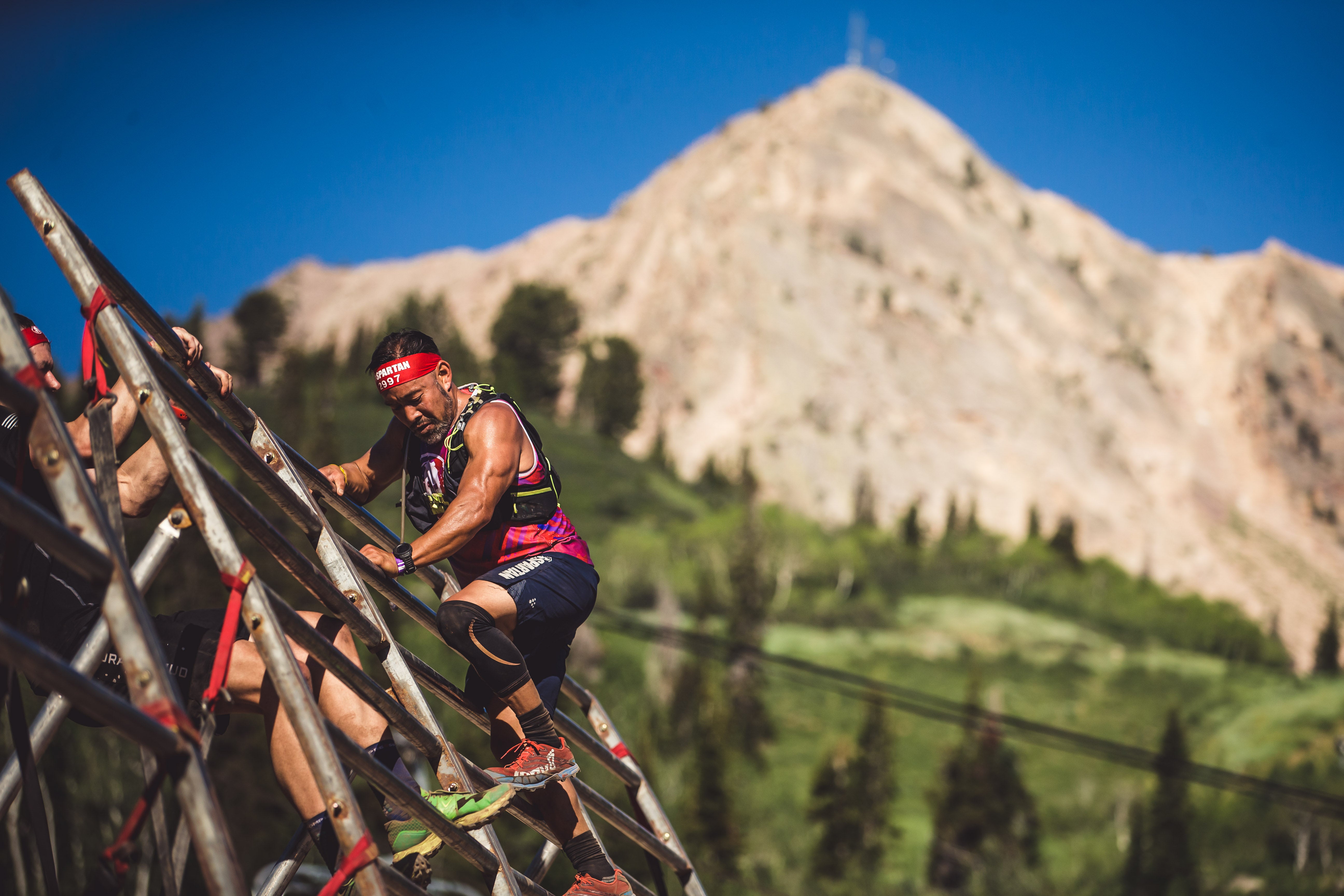 a racer climbs over the A Frame cargo in front of a mountain during a Spartan race