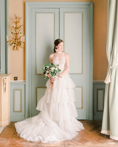 Bride in wedding gown holding a bouquet with silk ribbon by The Lesser Bear Photo by Mary Kate Steele in Chateau de Bonneval 