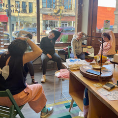 A group of teachers sitting in folding chairs around a store. They are each bending their head to the left and holding it to stretch their necks.