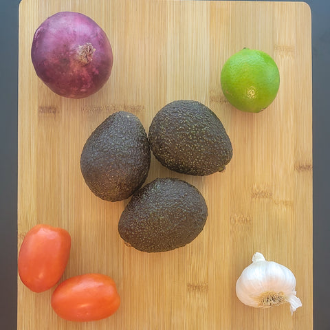 Guacamole ingredients: avocados, red onion, lime, roma tomatos, and garlic