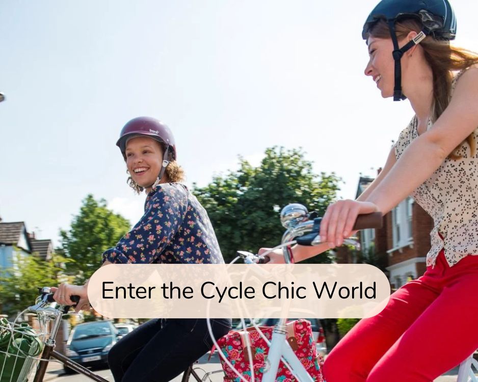 Enter the Cycle Chic World: two smiling women wear cute helmets and ride bikes next to each other.