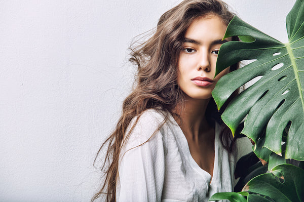 Young beautiful brunette with long hair posing in Studio with tropical plant on isolated background