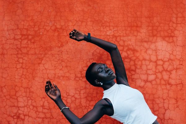 Beautiful dark skin woman hands up, eyes closed, like falling from a dream. Orange wall behind. 