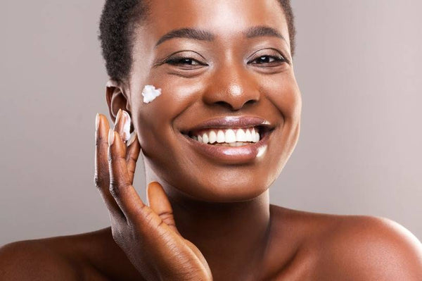 Woman of color applying moisturizer onto her cheek.