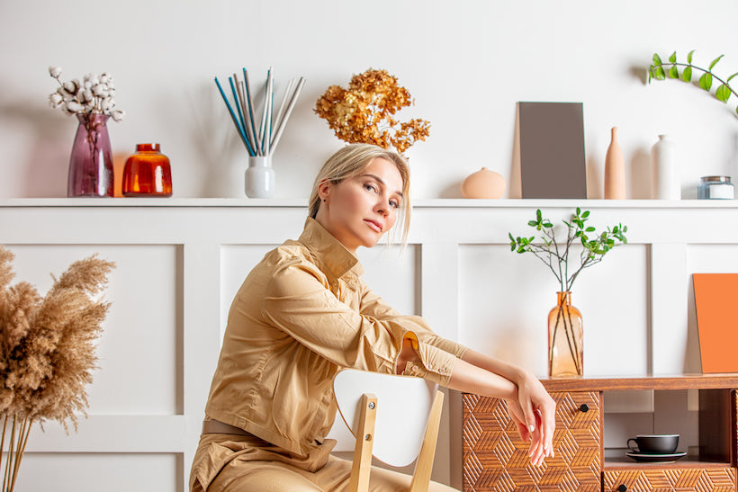 Portrait of a beautiful blonde woman sitting on a chair, in a beige suit against the background of an interior with decor in the form of vases, flowers, and furniture
