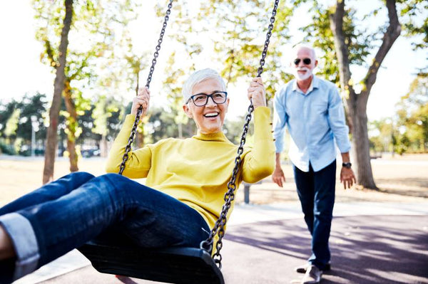 A man is pushing his wife on a swing and she's smiling