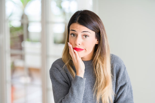 Woman with red lipstick and gray sweater holding her face in doubt