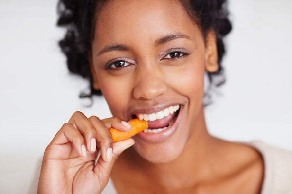 Happy young African American female eating a carrot