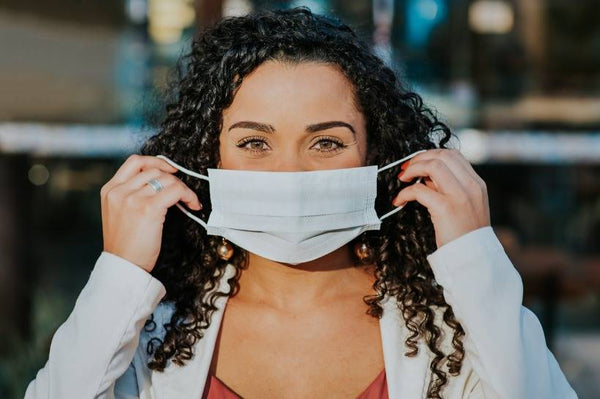 Woman outside with curly hair, putting on a protective mask