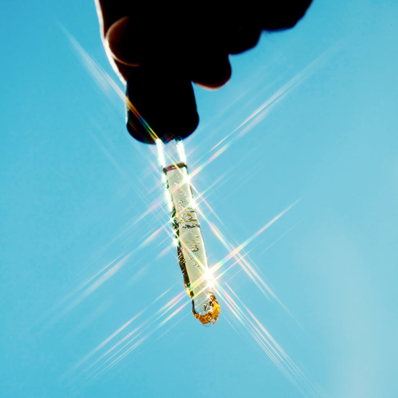 Hand holding shinny dropper with gold liquid. Blue sky as background.