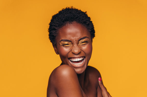 Dark skin woman laughing cheerfully against a yellow background