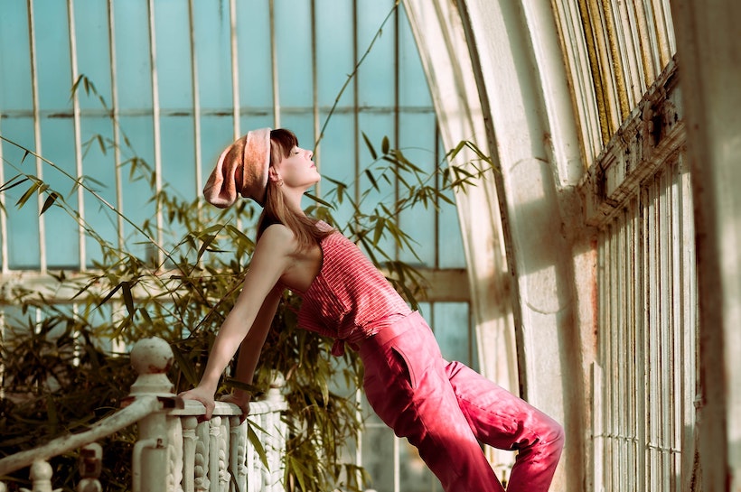 Young woman wearing red jumpsuit leaning on a fence of an old building