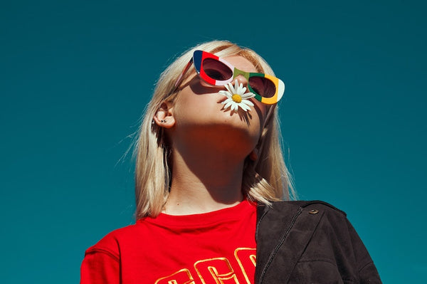 Blonde teenage girl wearing a red t-shirt, colorful sunglasses and flower on mouth looking up