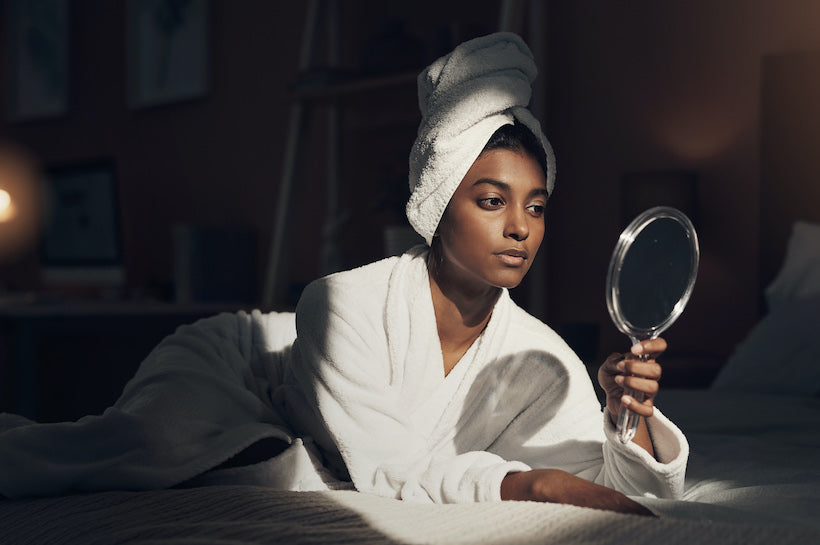 Shot of a young woman looking at herself in the mirror while going through her beauty routine at home