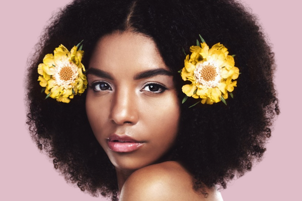 Curly-haired woman, gazing into the camera and wearing two yellow flowers in her hair