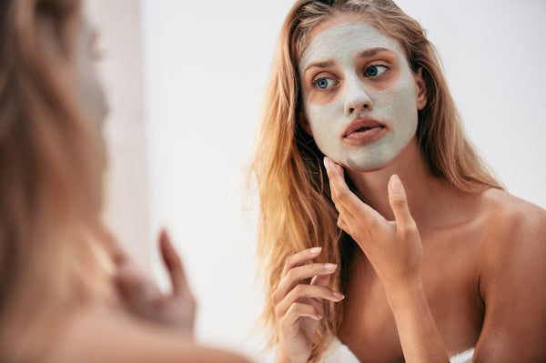 Woman with algae mask on her face looking at the mirror