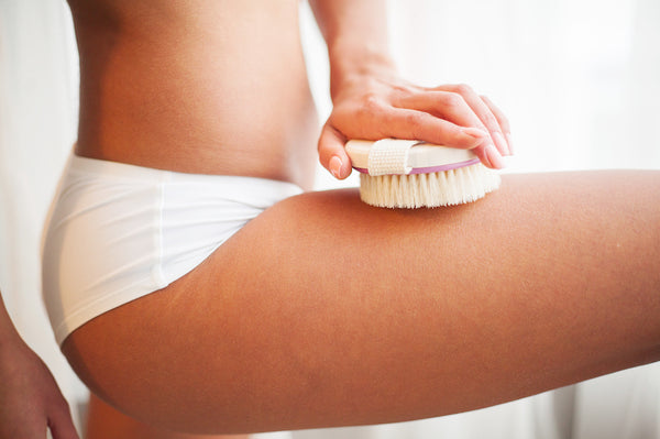 Woman's arm holding dry brush to top of her leg. Dry brushing