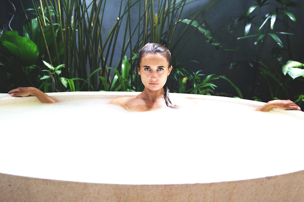 Woman inside a tub taking a milk bath with plants on the background