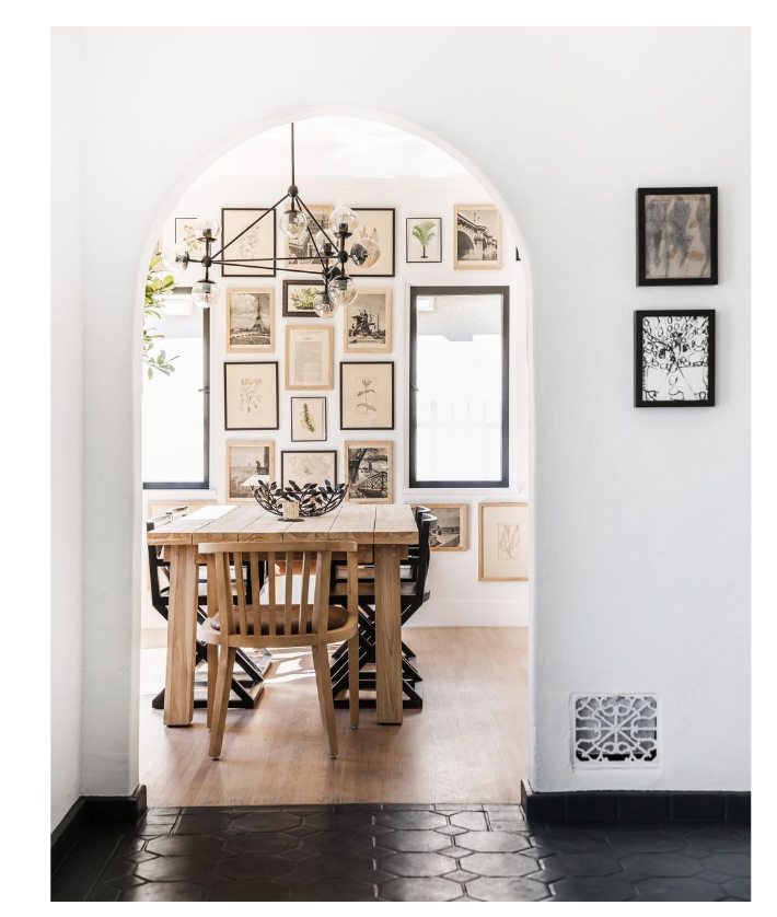 a cute little dining room with a wooden table, an arch entry way and a lot of art hanging on the wall