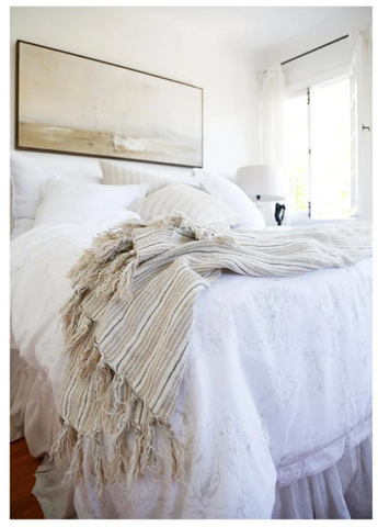 A corner of a light colored bed with a striped throw draping